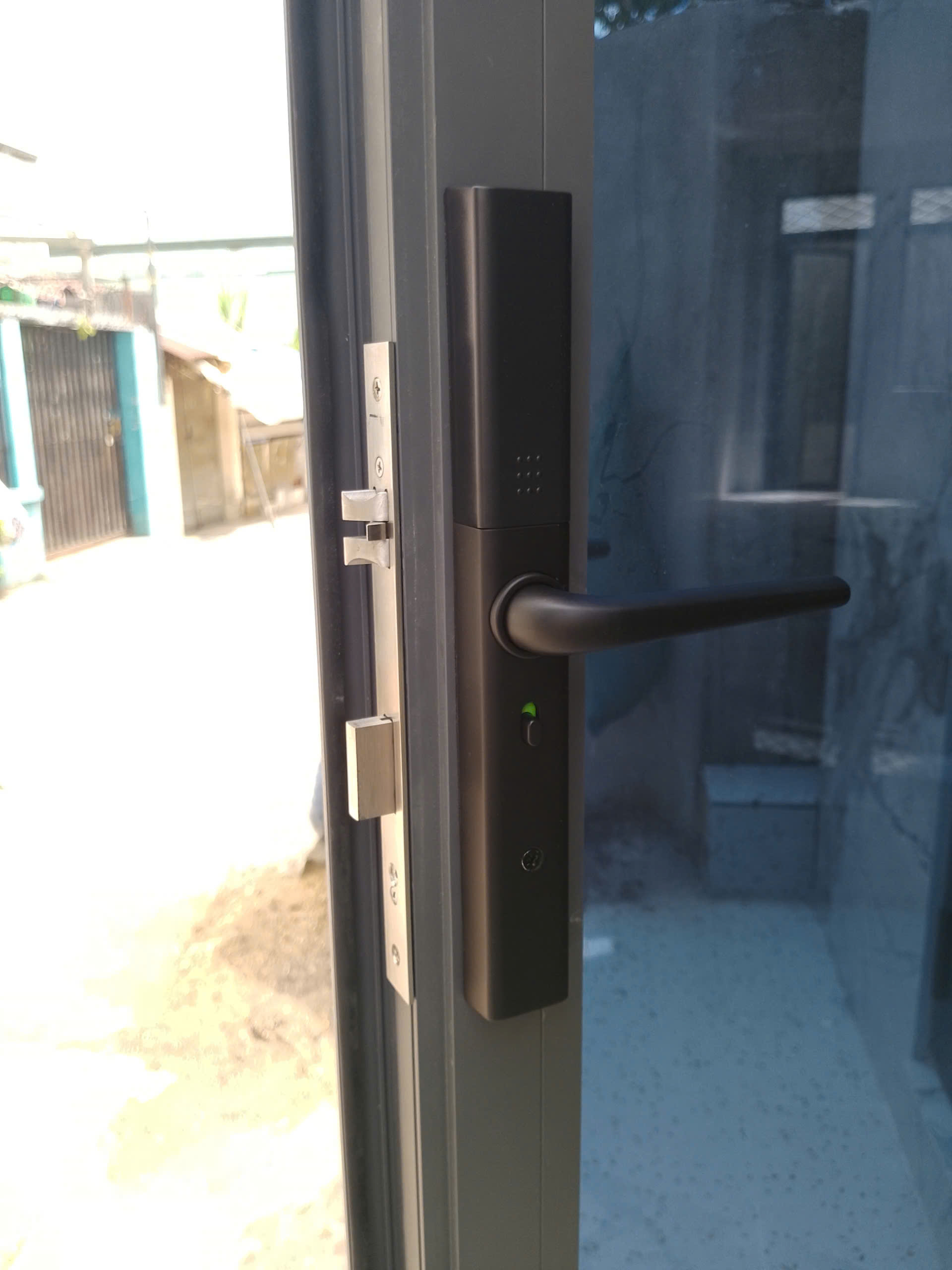 Mặt ngoài khóa vân tay Avolock AN-395-B trên cửa nhôm kính: thân khóa mỏng ôm khít đố nhôm, chốt thép ăn khớp gọn — ảnh lắp đặt thực tế