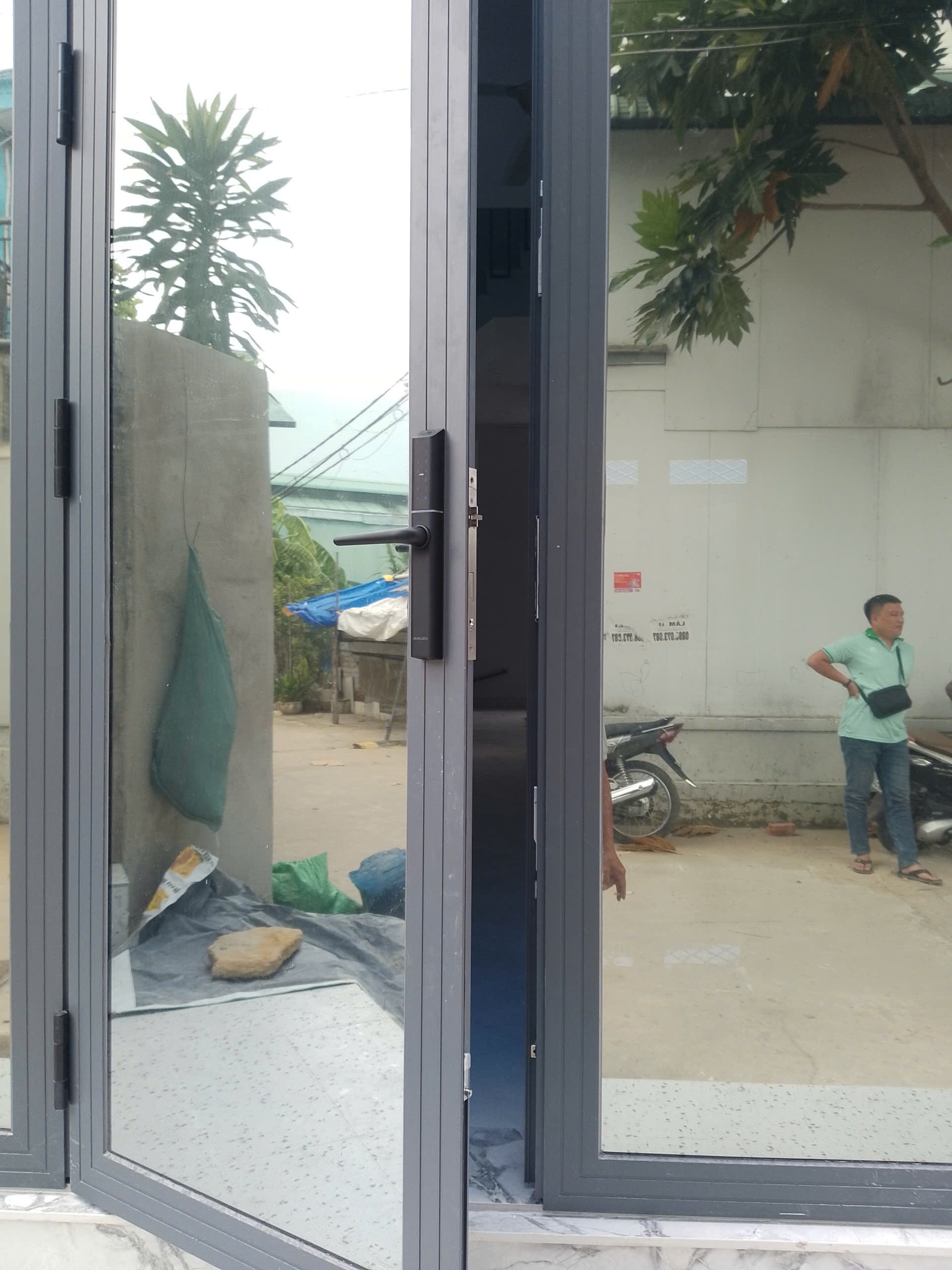 Tổng thể khóa vân tay Avolock AN-395-B trên cửa nhôm kính mở ra sân: gọn gàng, hài hòa với khung nhôm — ảnh lắp đặt thực tế