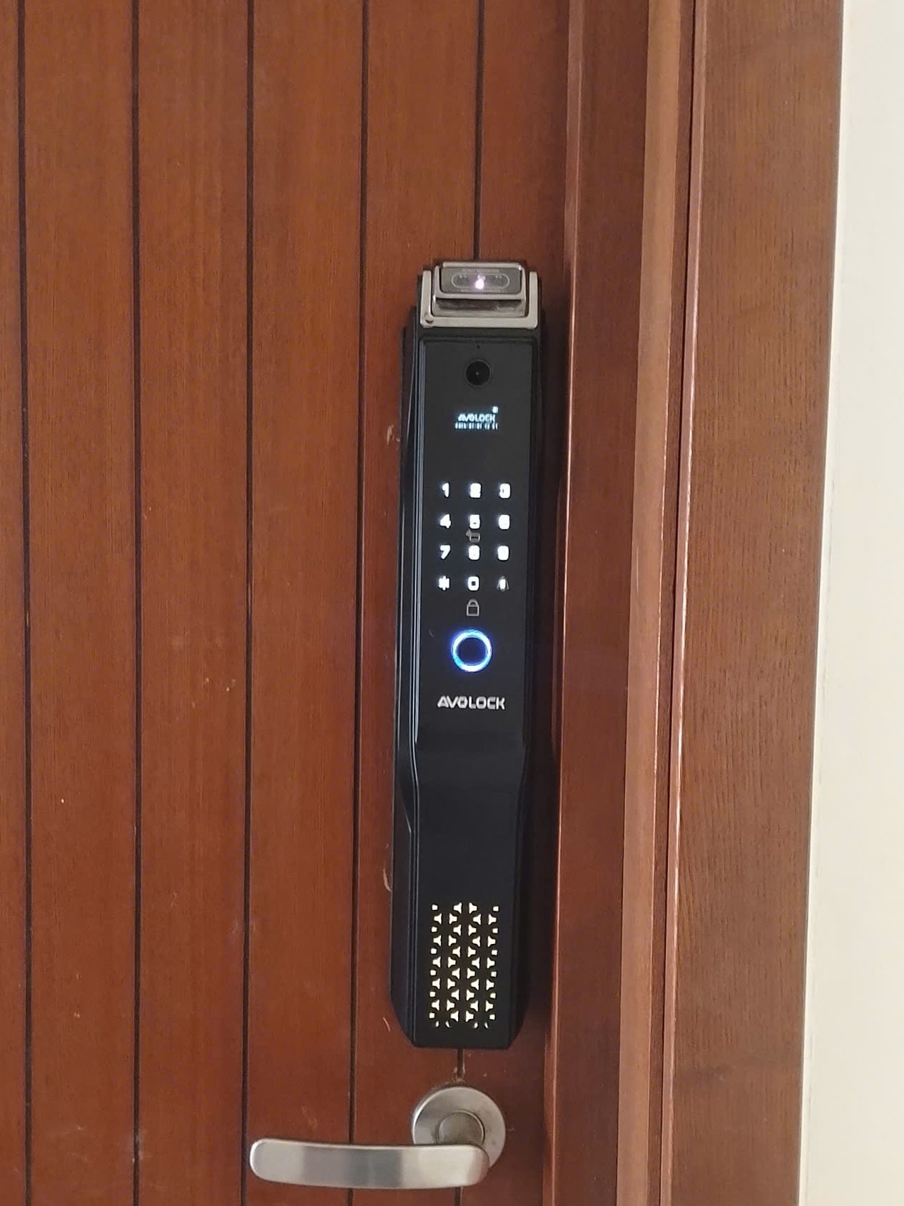 Khóa vân tay Avolock AL 76TFV lắp đặt thực tế trên cửa gỗ — mặt ngoài với Face ID 3D và bàn phím cảm ứng sáng