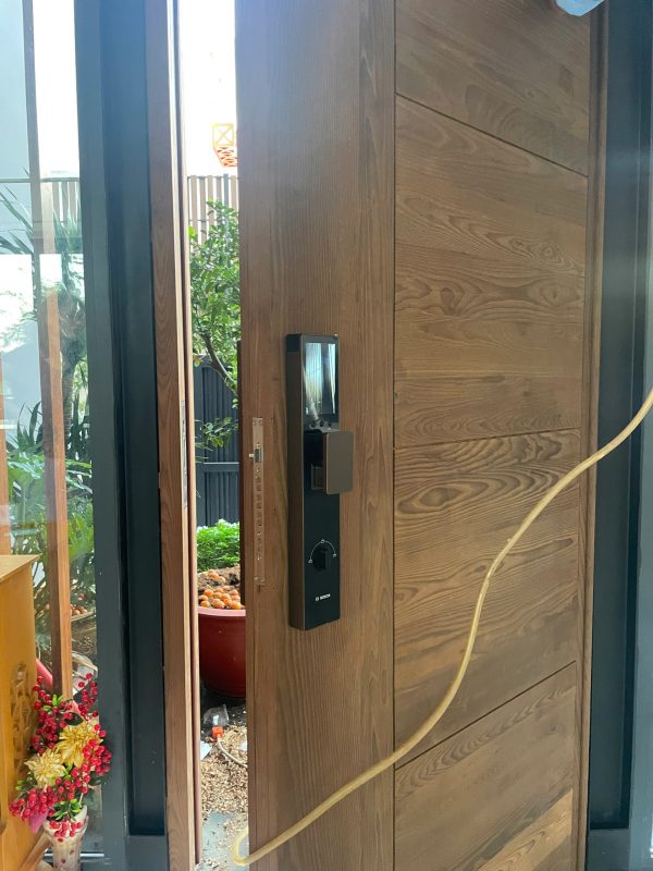 Khóa vân tay Bosch FU30 Plus Face ID lắp đặt thực tế trên cửa gỗ nhà phố — thân đen viền nâu đồng, tay đẩy kéo push-pull, camera nhận diện khuôn mặt