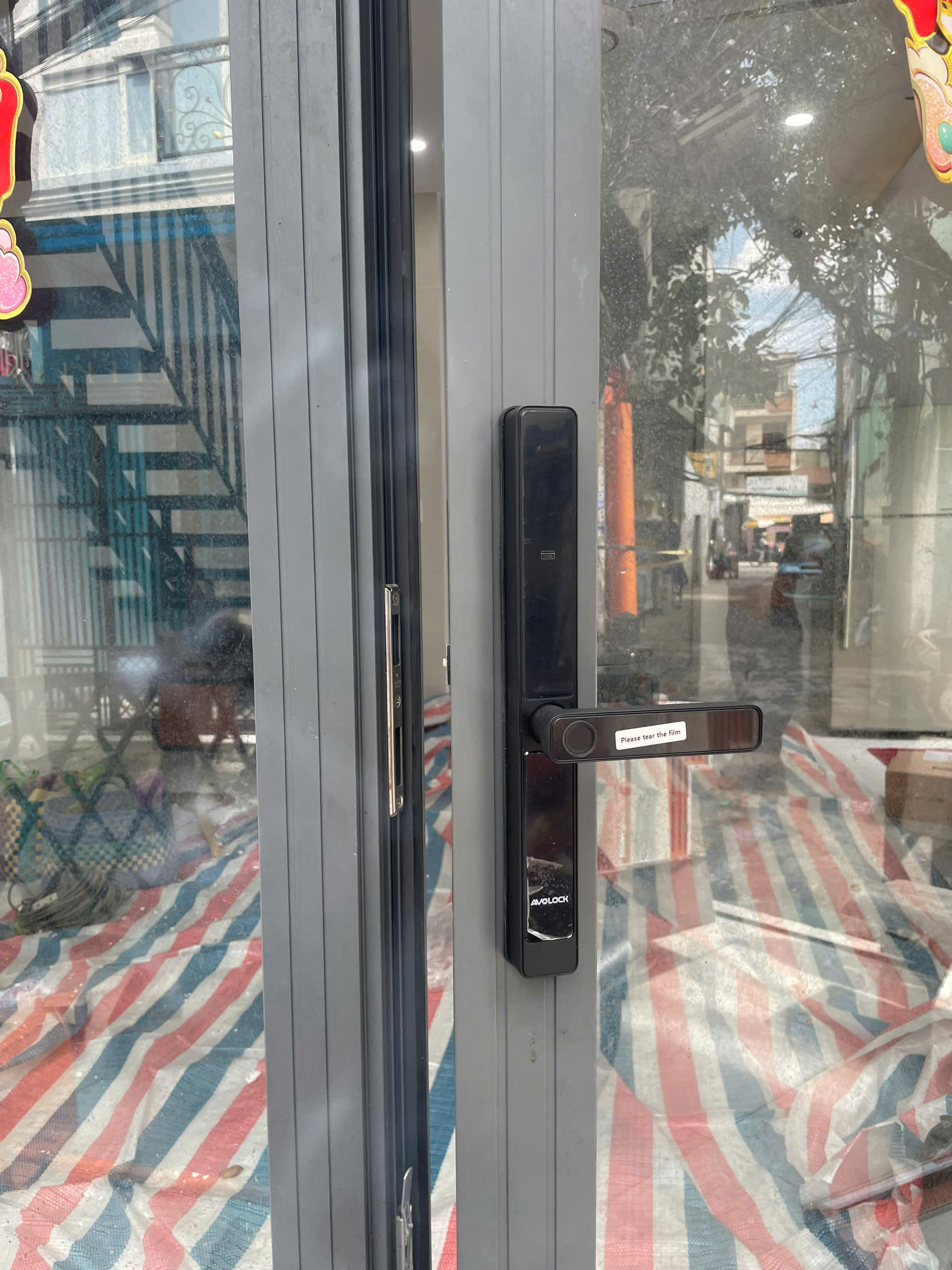 Cận cảnh mặt ngoài khóa vân tay Avolock AN-382 lắp đặt thực tế trên cửa nhôm kính, logo AVOLOCK