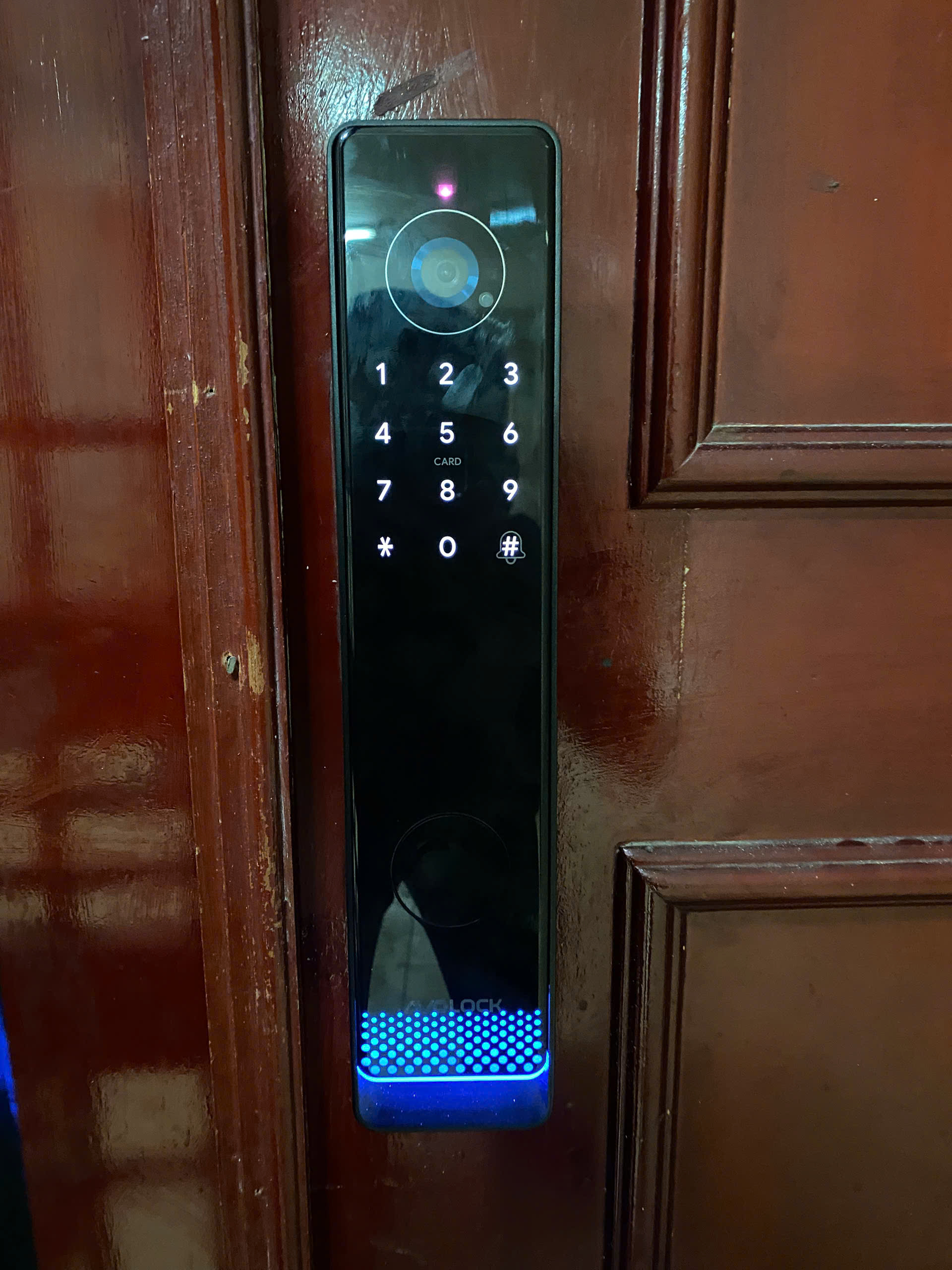 Mặt ngoài khóa Avolock AL-81 lắp đặt thực tế trên cửa gỗ với camera chuông hình và đèn báo trạng thái
